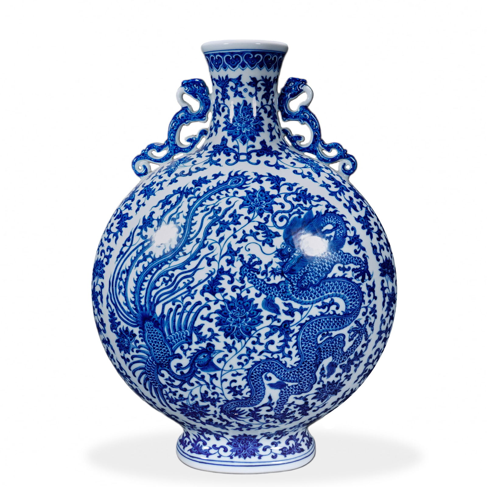 A BLUE AND WHITE 'DRAGON AND PHOENIX' MOON FLASK: A BLUE AND WHITE 'DRAGON AND PHOENIX' MOON FLASK H: 41 cm (16 1/8 in); W: 31 cm (12 1/4 in) The moon flask form provides a broad canvas for the depiction of dragon and phoenix in vivid cobalt blue. Th