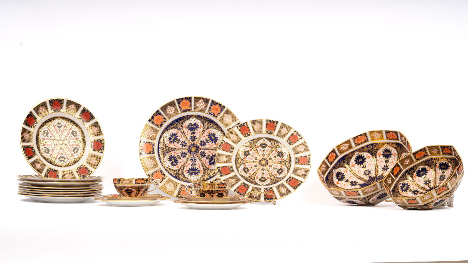 19 Pieces Royal Crown Derby Old Imari China Set: 19-piece Royal Crown Derby porcelain set in the iconic Old Imari Pattern 1128. The set includes an assortment of plates, cups, saucers, and bowls. The pattern is in a traditional Japanese-inspired mot