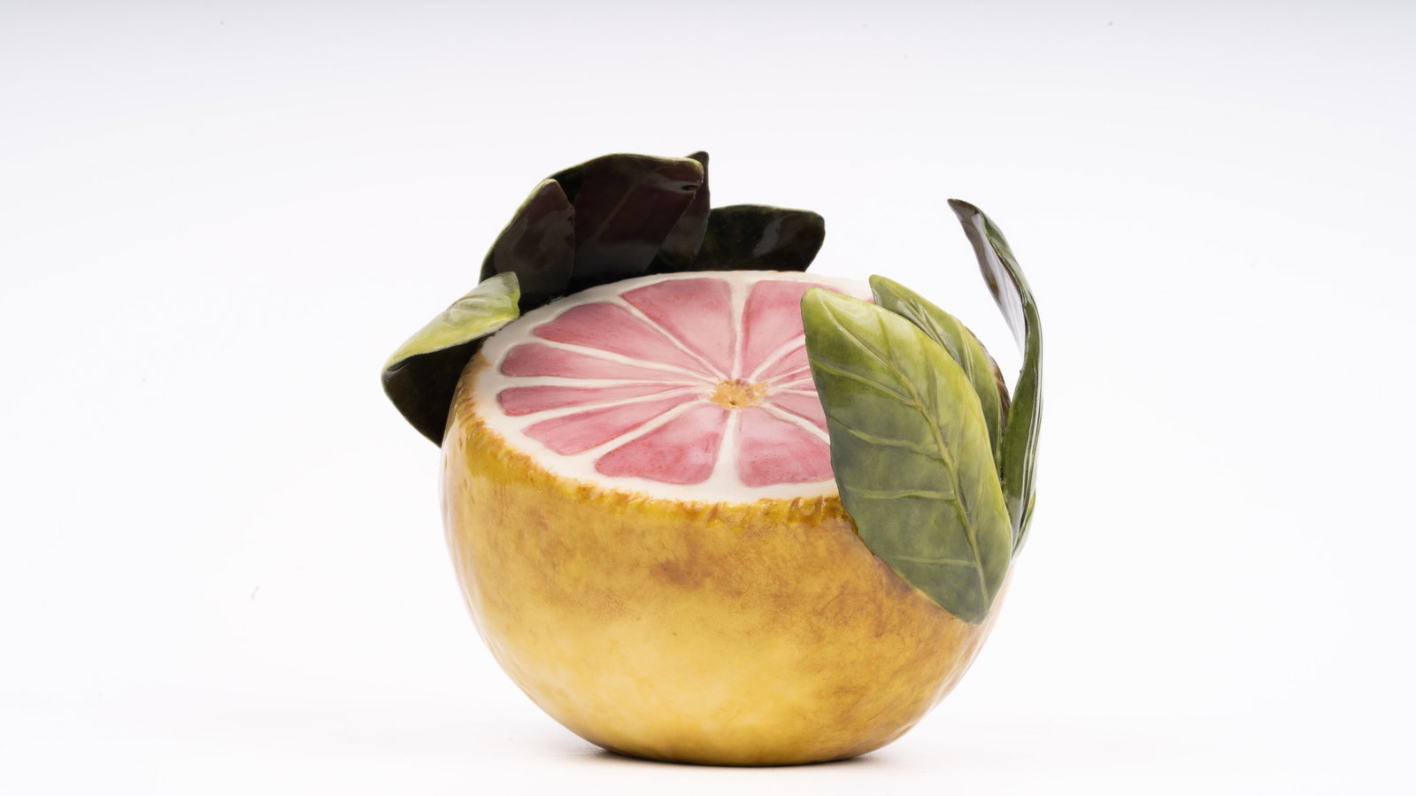 Katherine Houston Porcelain Painted Grapefruit: A lifelike hand-modeled porcelain sculpture by celebrated American artist Katherine Houston, depicting a halved pink grapefruit adorned with deeply veined glossy green leaves. Houston’s signature ap