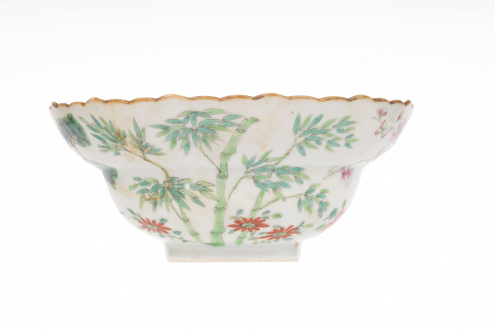 Chinese Famille Rose Porcelain Bowl Qing Dynasty Qianlong Period: Of scalloped form with gilt rim, delicately enameled in famille rose with alternating scenes of pine, bamboo, and flowering plants, emblematic of the "Three Friends of Winter," symbols of resilience a