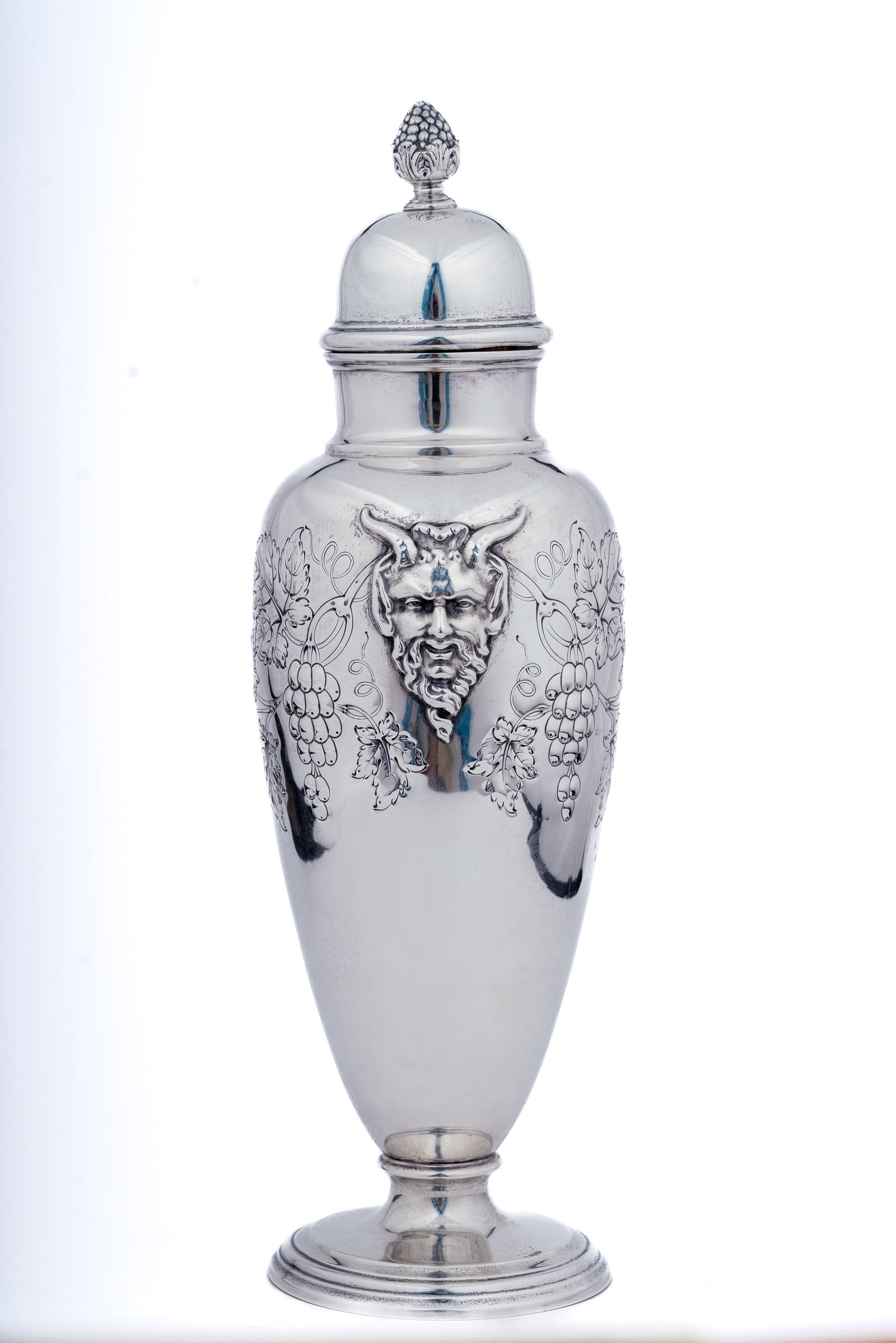 International Sterling Silver Bacchus Cocktail Shaker: A finely crafted sterling silver cocktail shaker by International Silver Co., featuring bold repousse decoration of Bacchus, the Roman god of wine, surrounded by grapevines and foliage. The shaker has