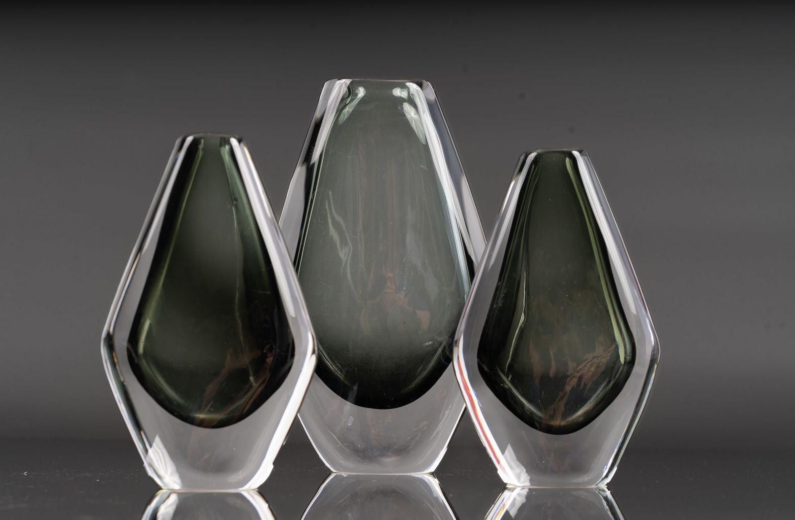 (3)Nils Landberg by Orrefors Smoked Glass Sculptural Vases: A group of three modernist Nils Landberg by Orrefors vases, each of heavy cased glass with smoked gray interiors and clear faceted exteriors, displaying the brand’s characteristic Scandinavian restr