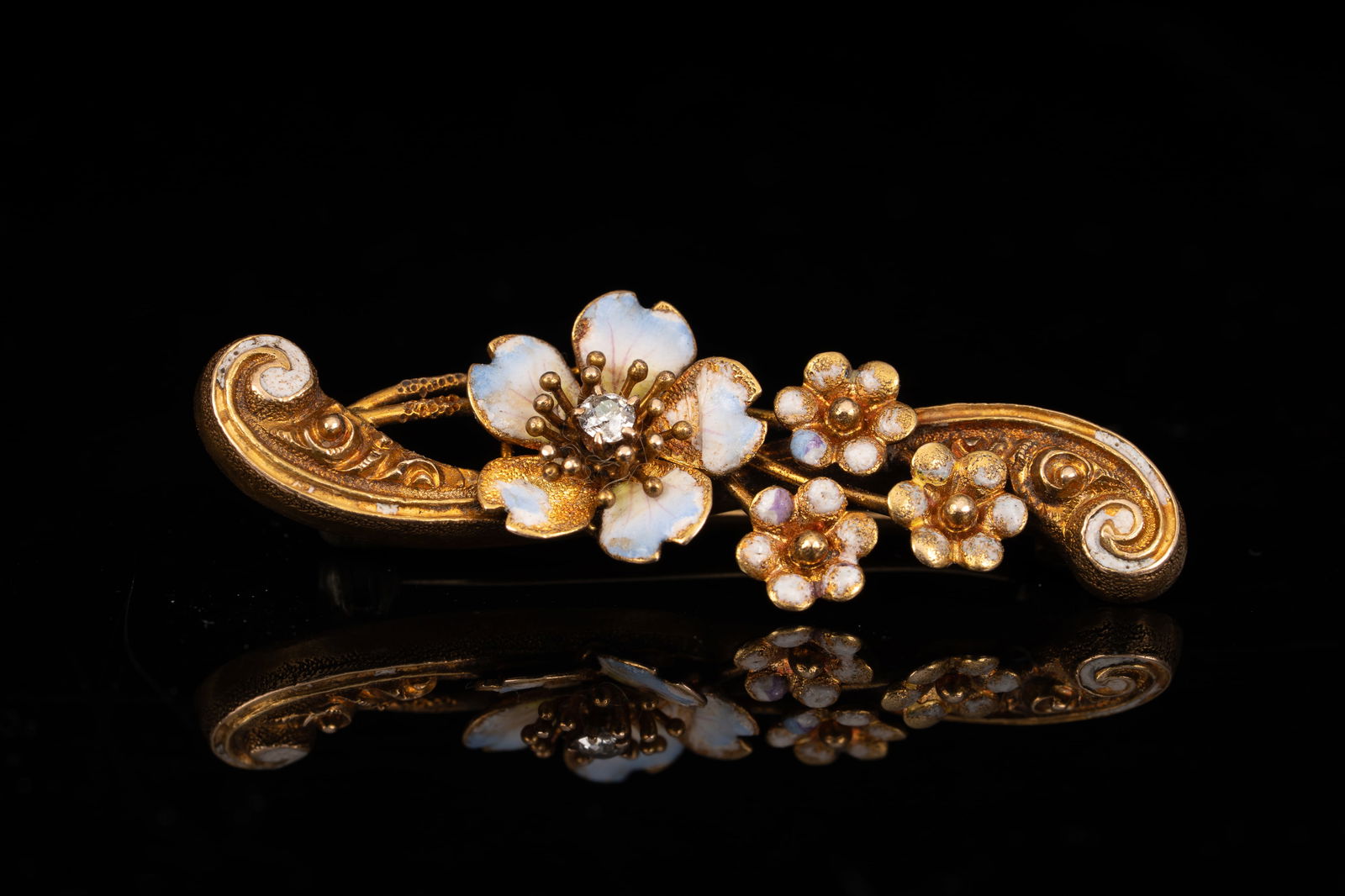 14K Yellow Gold and Enamel Floral Brooch Pin: A finely detailed 14K yellow gold floral brooch featuring a central white enameled blossom accented by a small diamond, surrounded by smaller enameled flowers and scrollwork. The enamel displays soft
