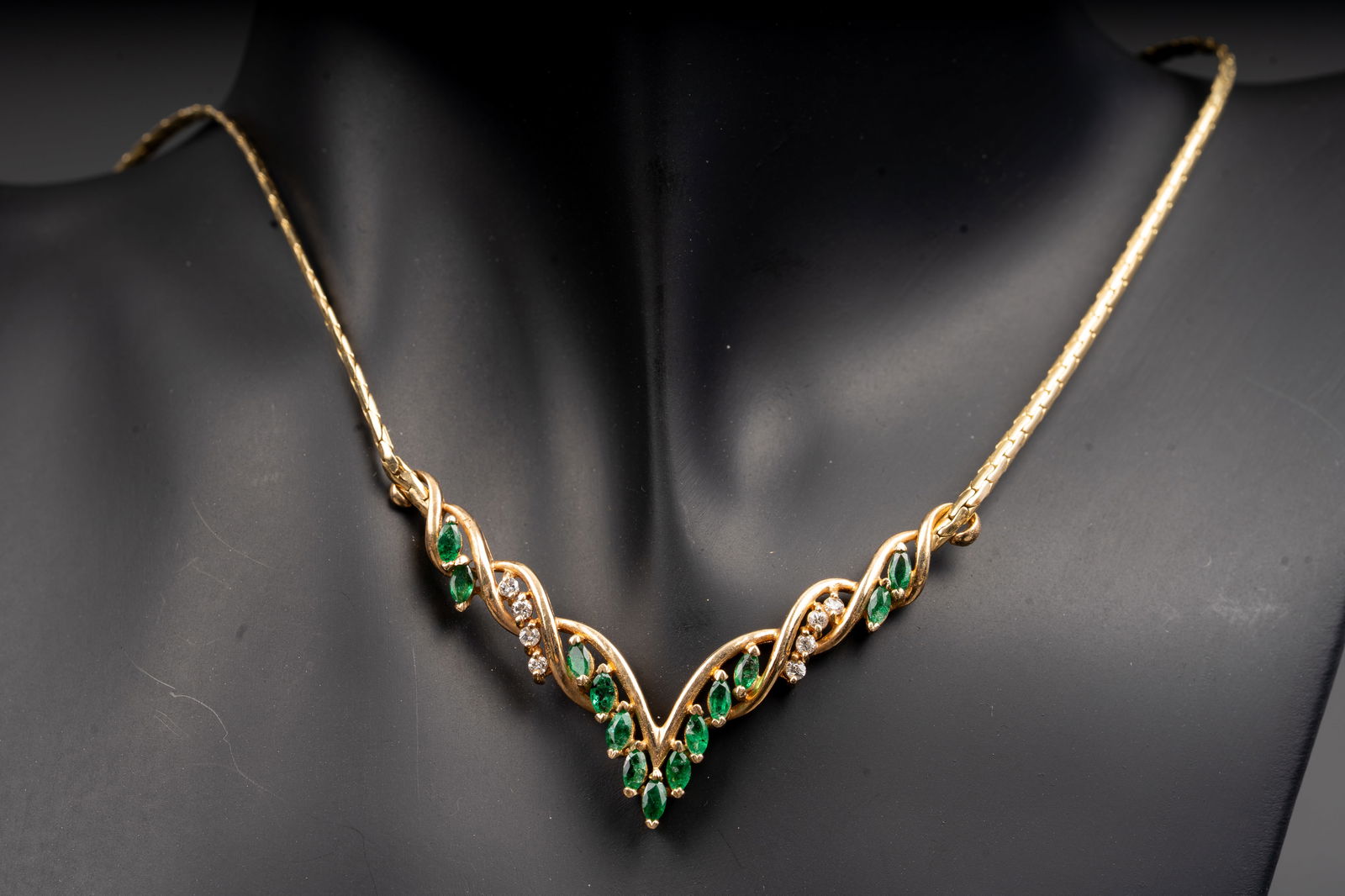 14K Yellow Gold Necklace with Emeralds and Diamonds: An elegant 14K yellow gold necklace featuring a graceful V-form design with interlacing scrollwork set with marquise-cut emeralds and round-cut diamonds. The emeralds, each measuring approximately 3.8