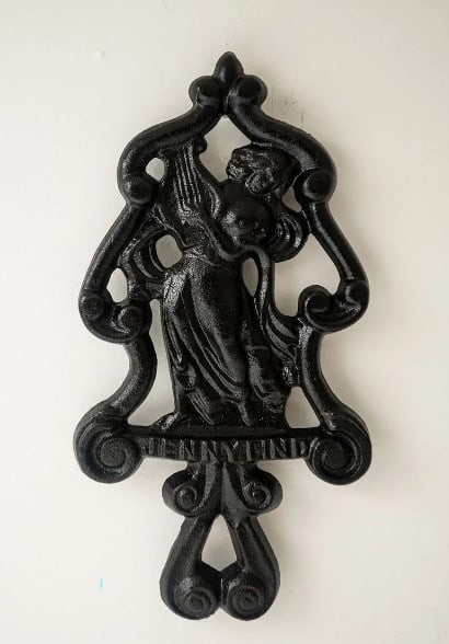 Cast Iron Trivet - Jenny Lind - 1930s: Material Culture: A Cast Iron Raised Figural Trivet with a rendition of Jenny Lind playing the harp, made between 1930 and 1940. Three solid feet on the underside. This item is featured in several edu