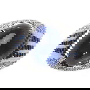 A SAPPHIRE AND DIAMOND RING: Set with an oval cabochon-cut sapphire measuring approximately 14.6 × 11.9 mm, within a pavé-set diamond surround, accented by channel-set calibré-cut sapphires on the shoulders, mounted in 18K whi