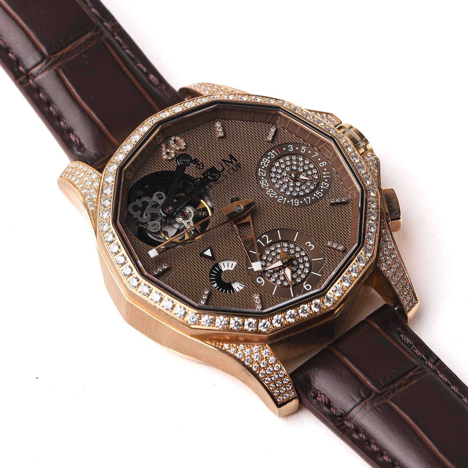 CORUM ADMIRAL'S CUP TOURBILLON GMT: The Corum Admiral's Cup Tourbillon GMT is an exquisite timepiece crafted in 18K rose gold, featuring a distinctive twelve-sided case set with brilliant-cut diamonds. The skeletonized dial showcases a