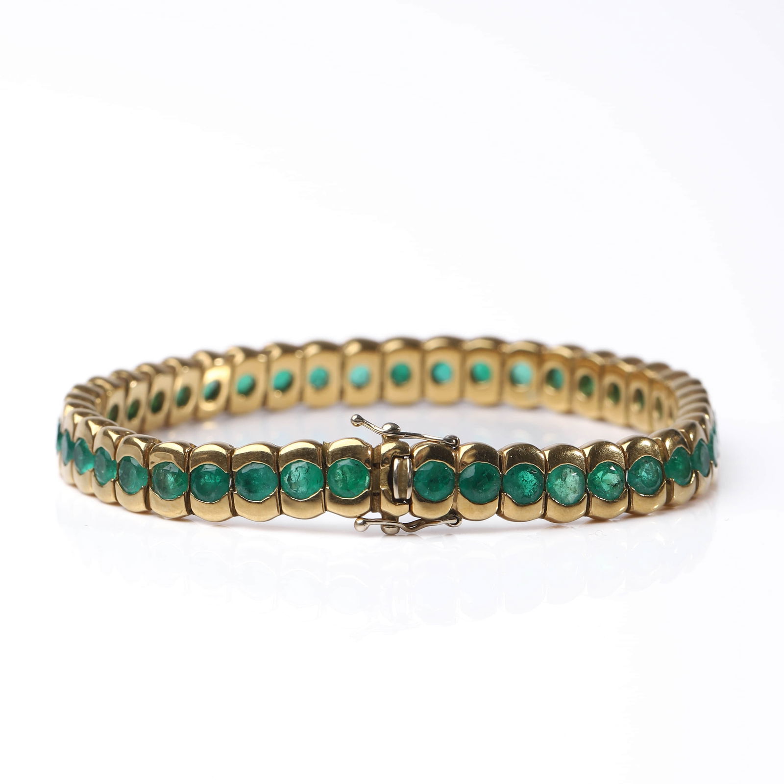EMERALD AND GOLD LINE BRACELET: Dimensions: Length: 18 cm; Weight: 30.6 g Description: An elegant line bracelet crafted in yellow gold, set with a continuous row of bright green emeralds in rounded bezel-style links that create a