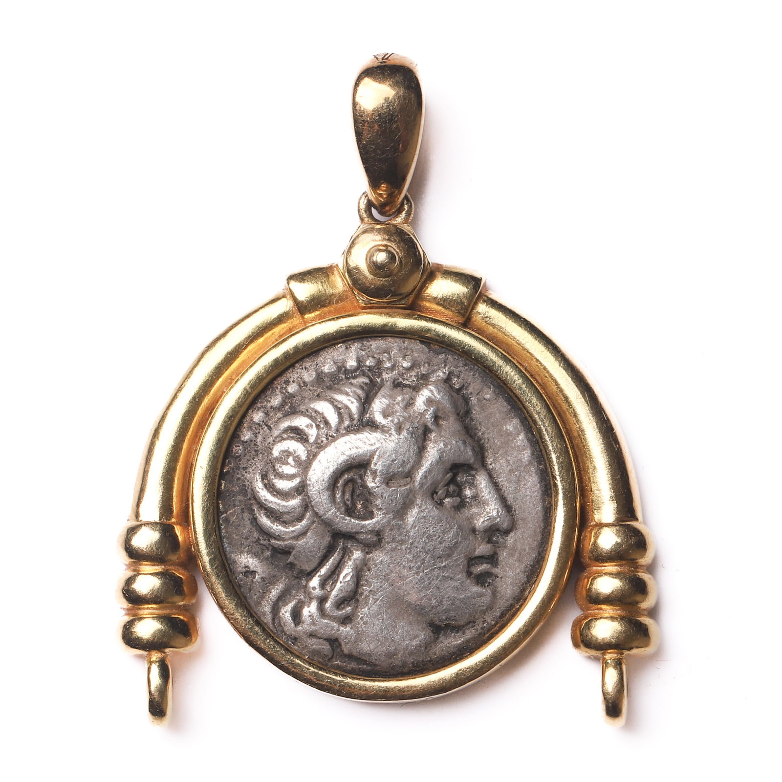 A GREEK SILVER COIN PENDANT OF ALEXANDER THE GREAT WITH RAM’S HORNS, SET IN AN 18K GOLD FRAME: Dimensions Height: 1 3/8 in. (3.4 cm), Width: 1 1/16 in. (2.7 cm) Weight:8.25 g Description A finely crafted pendant set with a silver coin depicting Alexander the Great with ram’s horns,