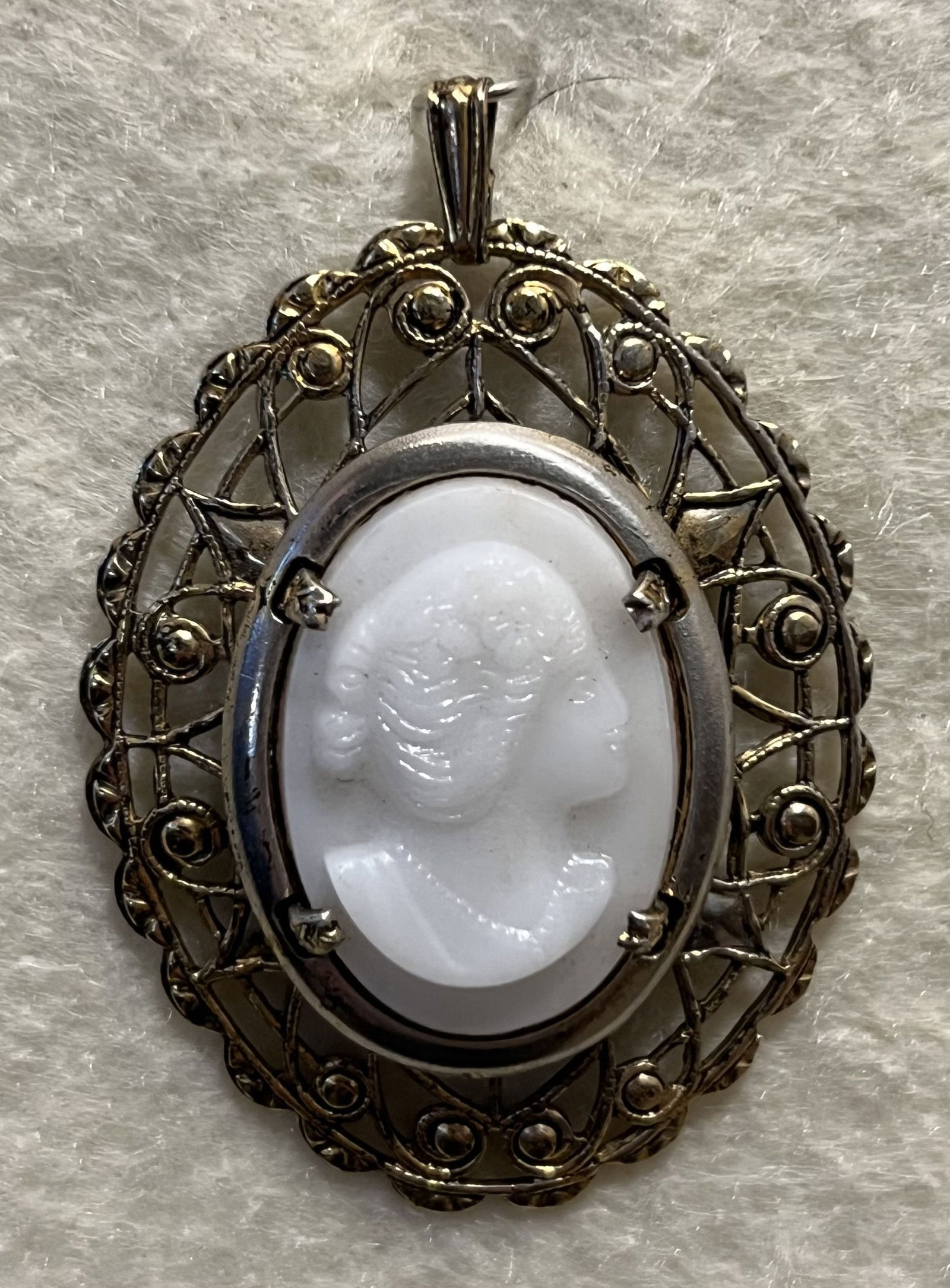 Oval White Glass Cameo Pendant: The attractive oval white glass cameo pendant is surrounded with almost a .5" decorative border of goldtone design. It's in good condition would add a touch of class to any outfit. (1.5" diameter) (1l