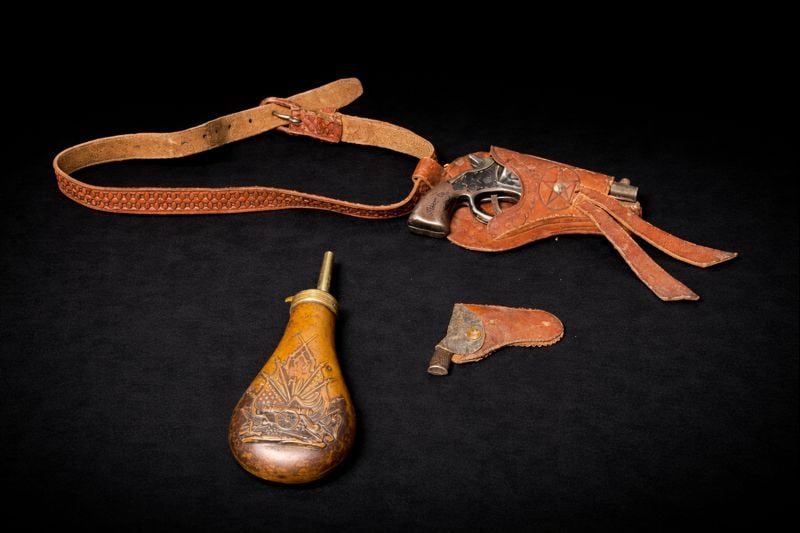 Western leather holster lot w/ holster/strap, miniature revolvers and decorative powder flask: Western leather holster lot 29” holster/strap, miniature revolver 6 1/4”L, miniature revolver 3 3/4”L, decorative powder flask 8”H x 3 1/2”W