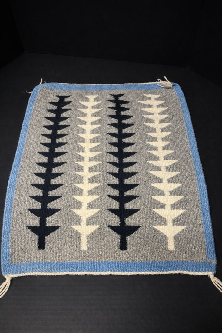 Handwoven Southwestern / Navajo-Style Wool Textile or Small Rug: gray field with repeating stepped tree/arrow motifs in black and ivory, framed by blue border; hand-loomed wool construction with corner tassels; geometric Native American–inspired design suitable