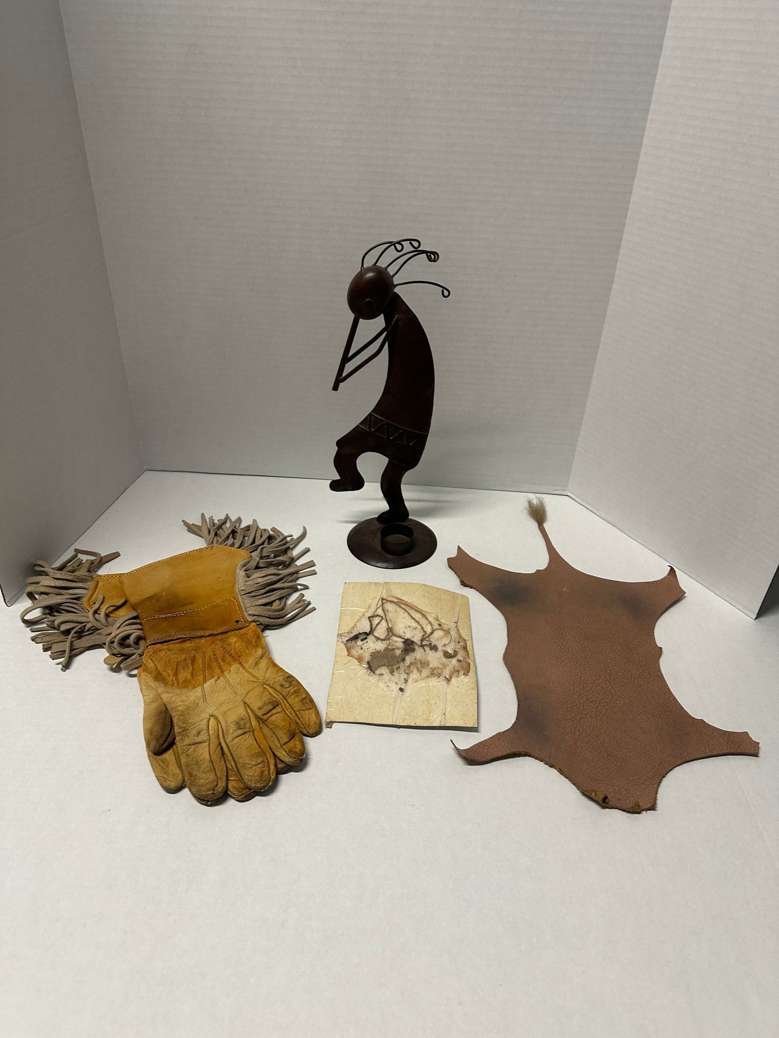 Southwestern Kokopelli figure, fringed leather gloves, hide and drawing lot (4 pcs): Southwestern lot of 4 including 13.5"H metal Kokopelli-style flute player figure, pair of approx 13"L fringed leather work gloves, tanned leather hide approx 19"L x 6"W with tail tip, and small primit
