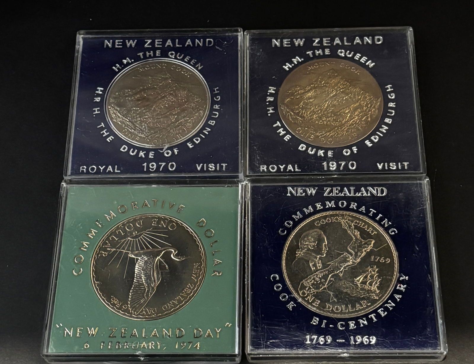 New Zealand $1 Commemorative Coins 1969–1974 (4): Group of four New Zealand One Dollar commemorative coins in original hard plastic presentation cases with colored velvet inserts. Includes: 1969 Cook Bi-Centenary (1769–1969), 1970 Royal Visit H.M.