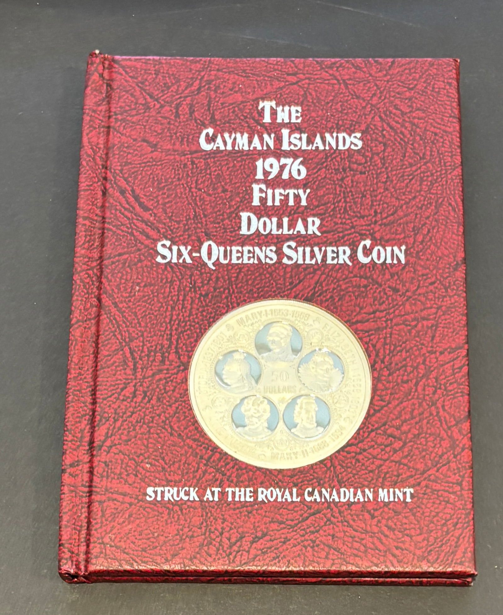 1976 Cayman Islands $50 Six Queens Sterling Silver Proof Coin In Book: 1976 Cayman Islands Fifty Dollar Six-Queens commemorative proof coin struck at the Royal Canadian Mint and housed in original red book-style presentation holder with certificate of authenticity. Large