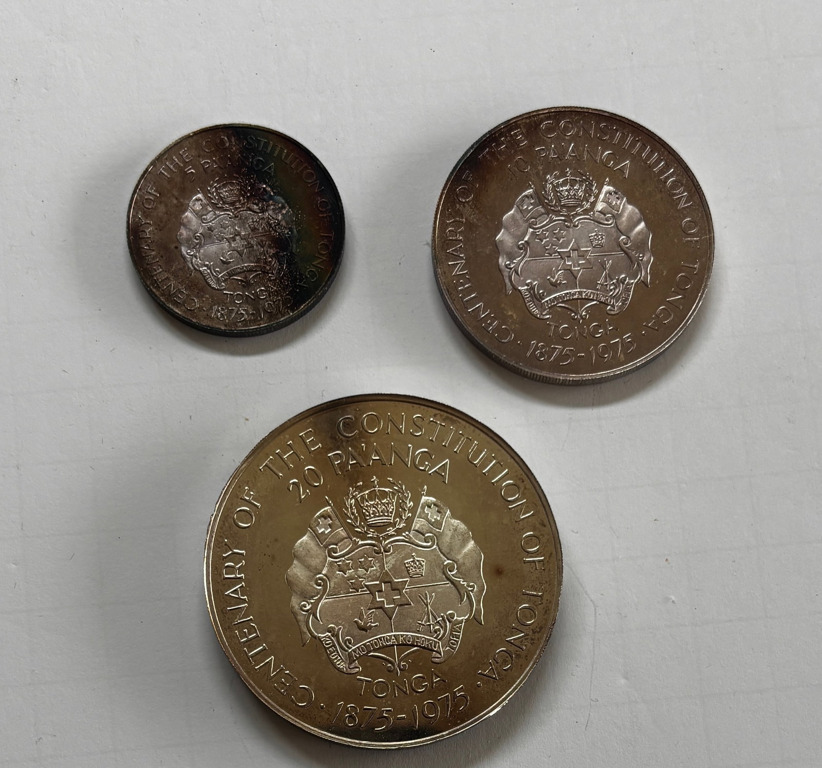 Tonga Constitution Centennial Commemorative Coin Trio: Group of three Tonga commemorative coins issued for the centenary of the Constitution of Tonga, dated 1875–1975, including 5 pa'anga, 20 pa'anga, and smaller denomination examples featuring the Tong