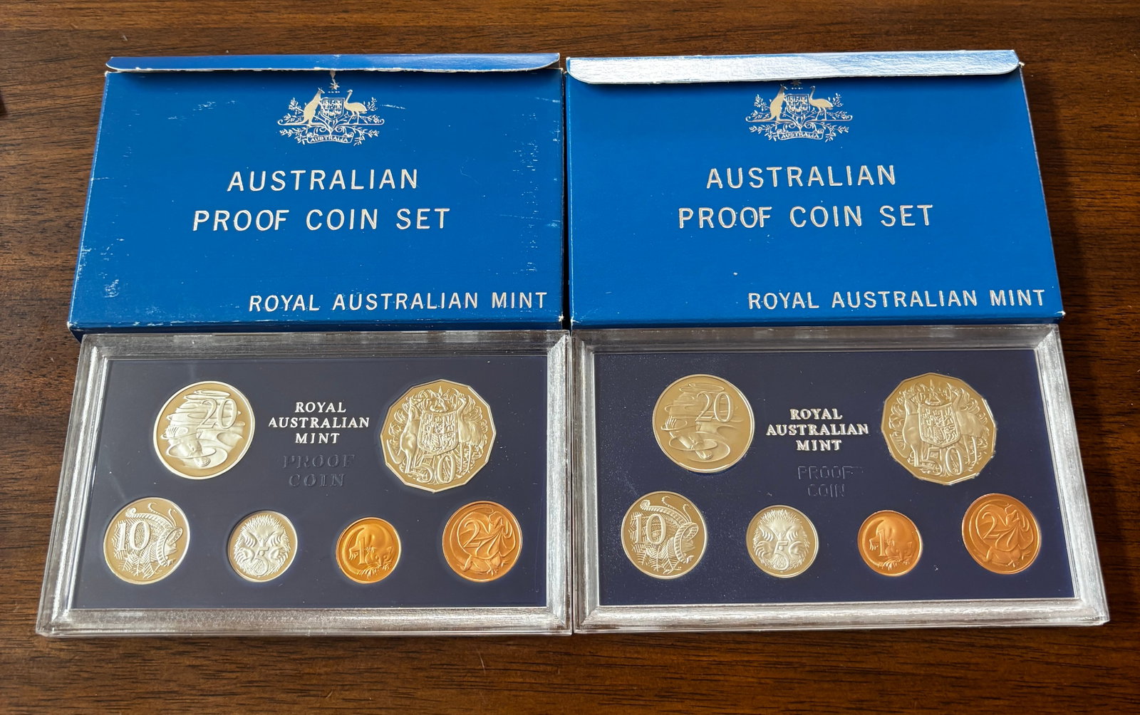 Two Royal Australian Mint Proof Coin Sets, 1981 and 1983, with Original Packaging: Collection of two official Royal Australian Mint Proof Coin Sets, dated 1981 and 1983. Each set is housed in its original hard plastic presentation holder and accompanied by its original blue Royal Au