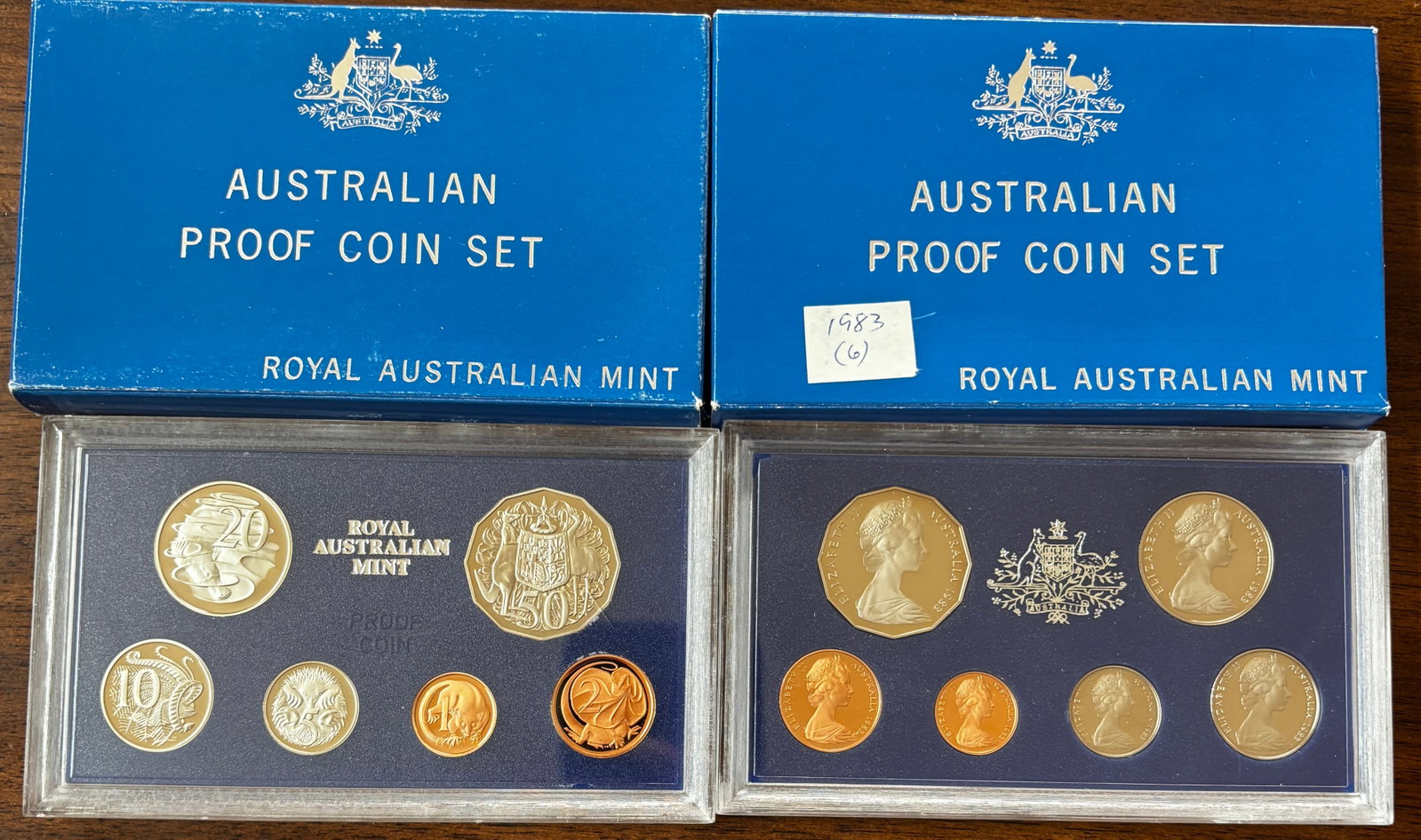 Two Royal Australian Mint Proof Coin Sets, 1983 and 1984, with Original Packaging: Collection of two official Royal Australian Mint Proof Coin Sets dated 1983 and 1984. Each set is housed in its original hard plastic presentation holder and accompanied by its original blue Royal Aus