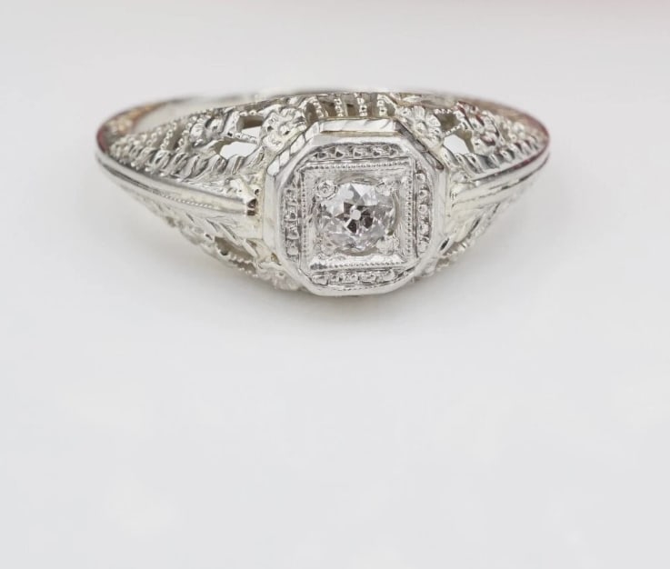 Art Deco 14k White Gold Natural Diamond Filigree Engagement Ring Sz 5.75 RG3522: This beautiful antique ring features a natural diamond solitaire set in a domed elegant mount with gorgeous filigree details and flower accents. The slim band provides a delicate comfortable fit.This