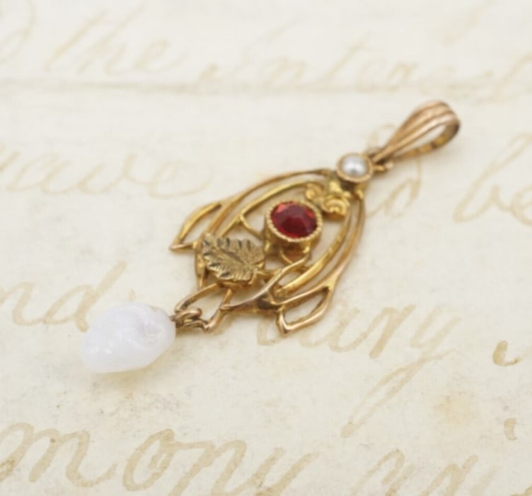 Vintage 10k Gold Lavalier Pendant Seed Pearl Red Glass Art Nouveau 1.25" PG1673: This beautiful vintage pendant features a faceted red crystal at the center of a delicate 10k gold frame with a leaf accent. A tiny seed pearl sits at the top, while a carved white pearlescent stone d