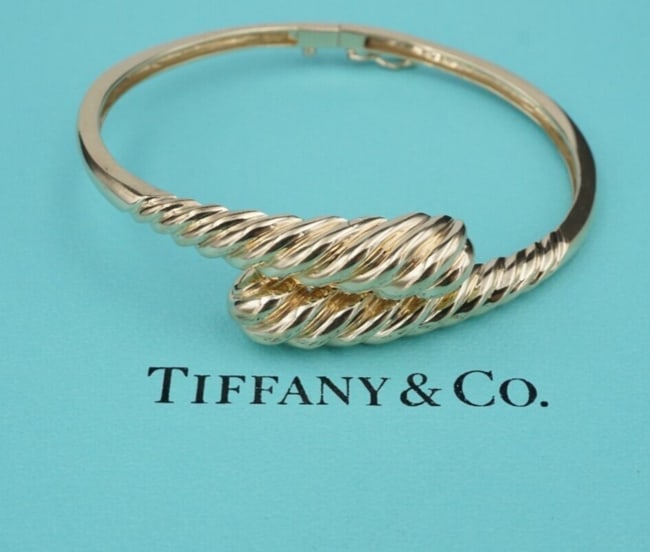Tiffany & Co. 14k Yellow Gold Bypass Bangle Bracelet 6.5" Hinge Retired BG974: This retired Tiffany & Co. bracelet features a classic 14k yellow gold bypass bangle design with a grooved texture on each tip. This timeless piece is the perfect addition to any Tiffany collection! M