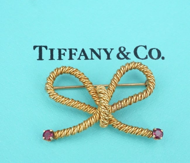 Tiffany & Co 18k Ruby Rope Bow Heart Twist Brooch Pin 0.99" Retired OG580: This gorgeous Tiffany & Co piece features a heart shaped bow motif with an ornate rope texture, and vivid red ruby finials. Crafted in rich 18k yellow gold, this stunning and highly versatile piece is