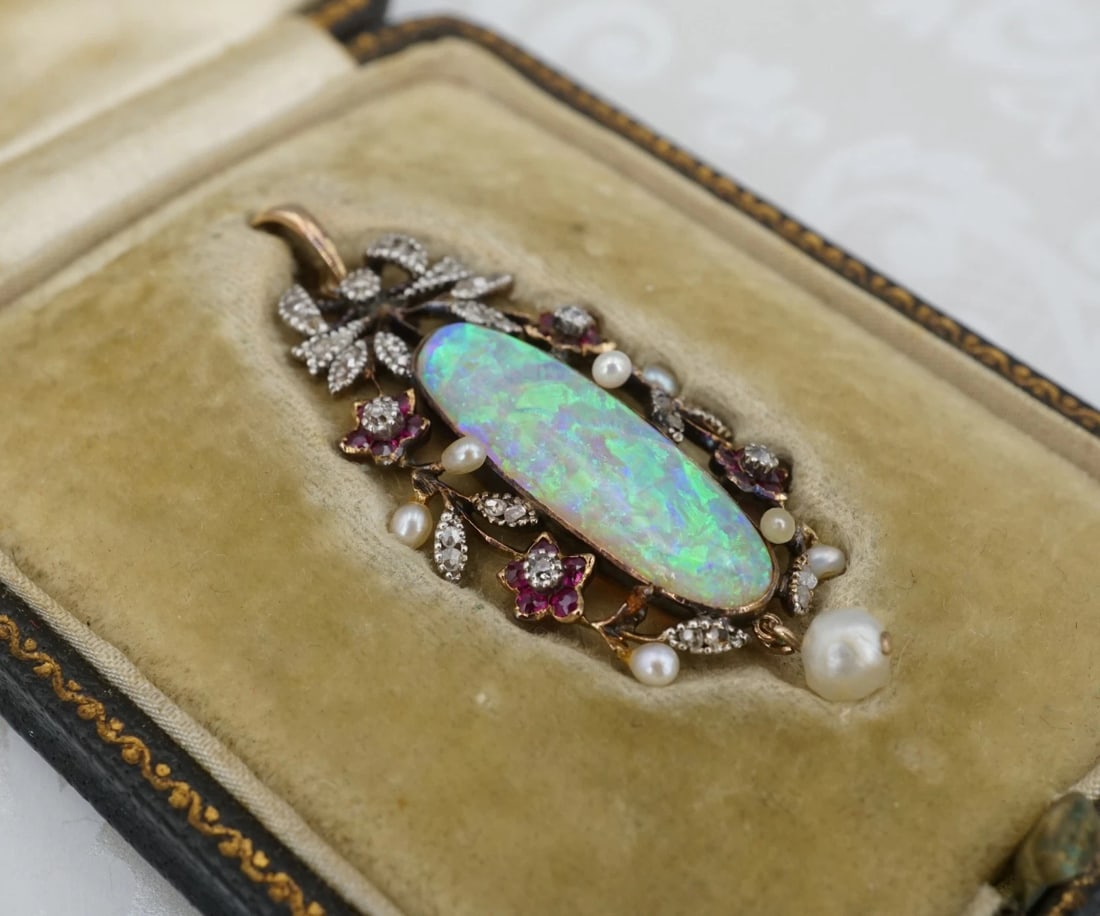 Antique 18k Opal Diamond Ruby Pendant Yellow Gold Fitted Box: This beautiful vintage piece features an elongated oval opal cabochon with a gorgeous play of color displaying flashes of blues and greens. The opal is surrounded by a floral wreath design of rubies, 