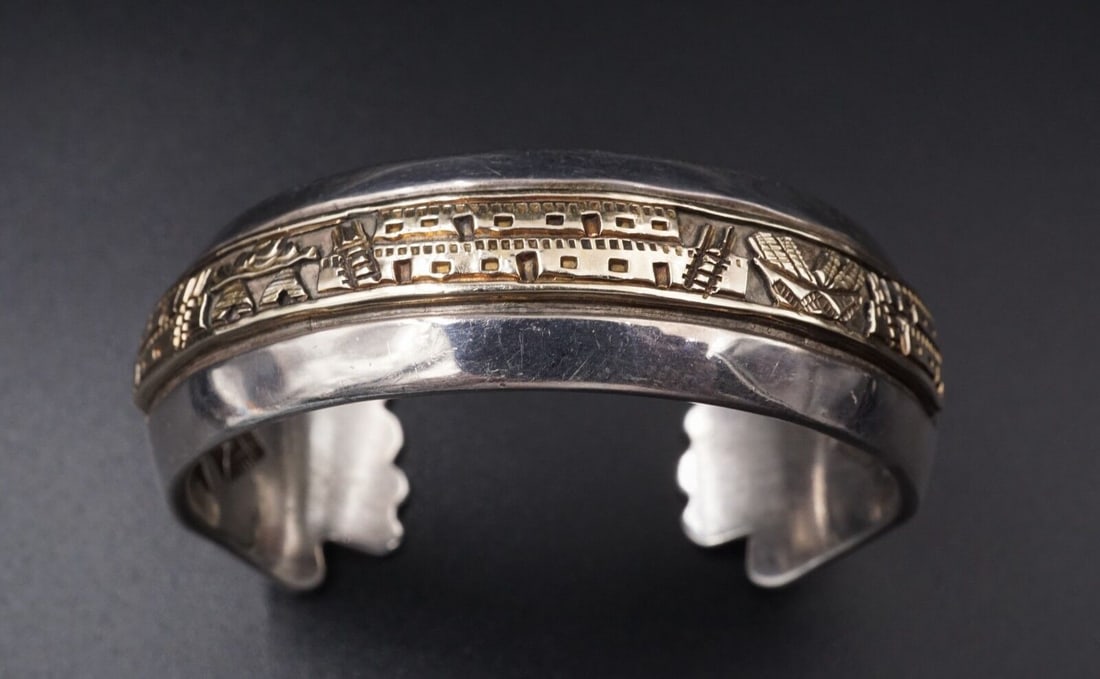 Navajo James Pioche Sterling Silver 14k Gold Pueblo Scene Cuff Bracelet BS1789: This elegant cuff bracelet is crafted and signed by Navajo artisan James Pioche. Featuring a beautiful polished curved surface of solid sterling silver, accented by a scene with Pueblo houses and bask