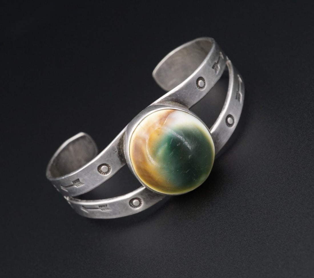 Harvey Era Vintage Silver Bracelet Operculum Shell Cuff Hand Stamped 6.5" BS2962: This vintage Fred Harvey Era cuff bracelet is crafted of sterling silver. It features a polished operculum shell set at the center with hand stamped sun and arrow accents. The natural patina showcases
