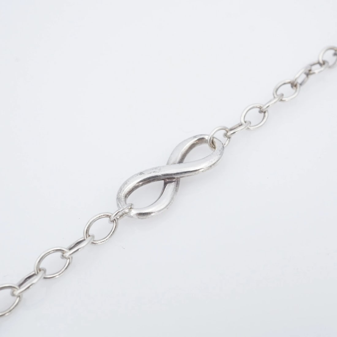Tiffany & Co. Infinity Chain Link Bracelet Sterling Silver 7" Retired BS3178: This retired Tiffany & Co. bracelet features a cable link chain design with a classic infinity charm fixed in the center. The bracelet fastens securely with a large lobster clasp. Metal Type: Sterling