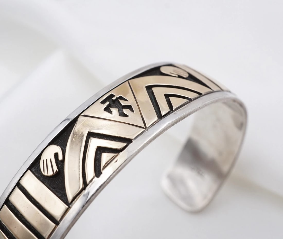 Mike Begay Overlay Cuff Bracelet Sterling Silver 14k Gold 7" 15mm Navajo BS3299: This bracelet from Navajo designer Mike Begay features a wide sterling silver cuff design embellished with a geometric, yellow gold overlay of arrows and hand motifs. Metal Type: Sterling Silver & 14k