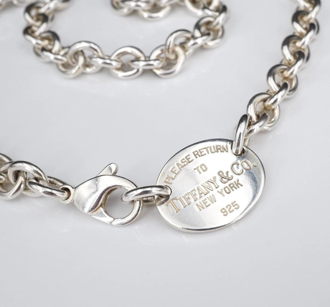 Return To Tiffany Oval Tag Charm Necklace Sterling Silver 16" Retired NS2401: This retired Tiffany & Co. necklace features a cable link chain design with a "Return to Tiffany" oval tag charm. The choker necklace fastens securely with a large lobster clasp next to the oval tag. 