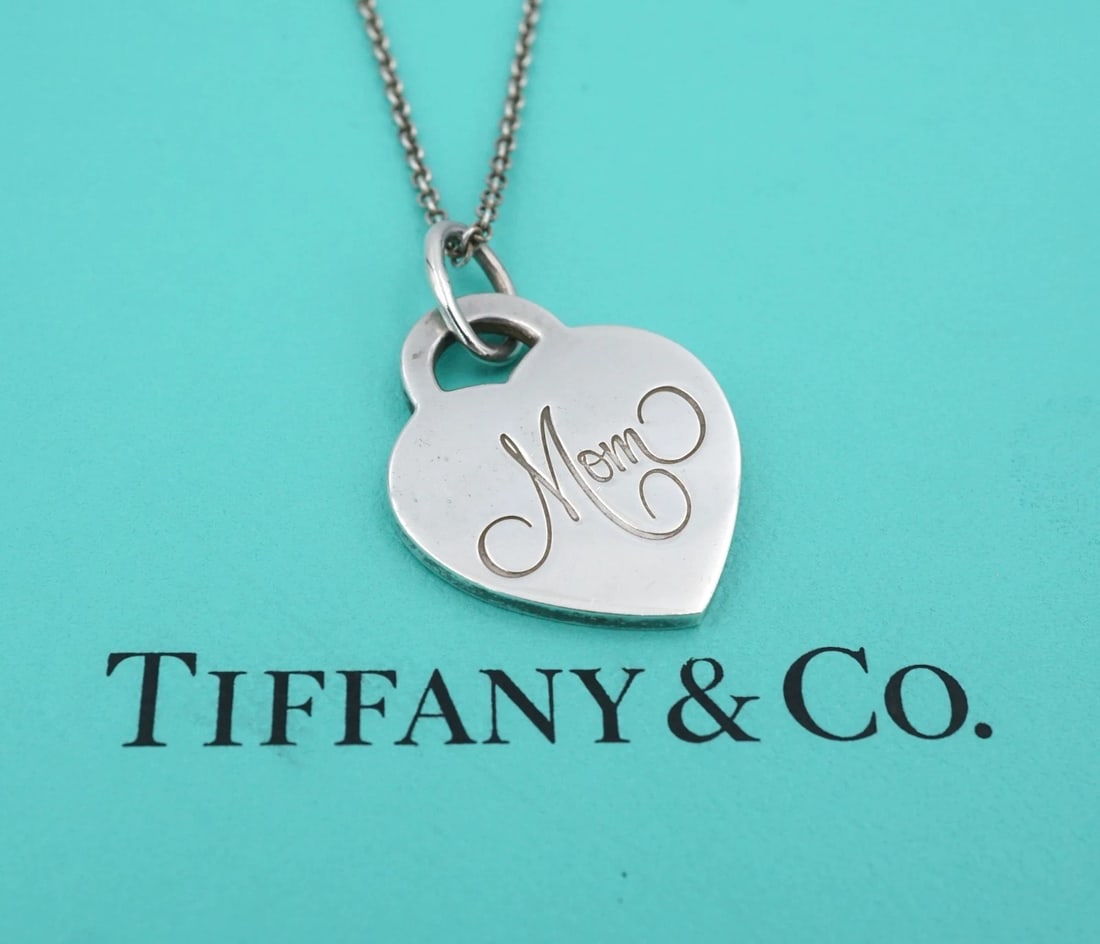 Tiffany & Co Mom Heart Tag Necklace Pendant Sterling Silver 18" Retired NS2426: This retired Tiffany & Co. necklace features a classic heart shaped pendant engraved with the word "Mom" in a script font. Suspended from a supple cable chain. Metal Type: Sterling Silver Notable Mark