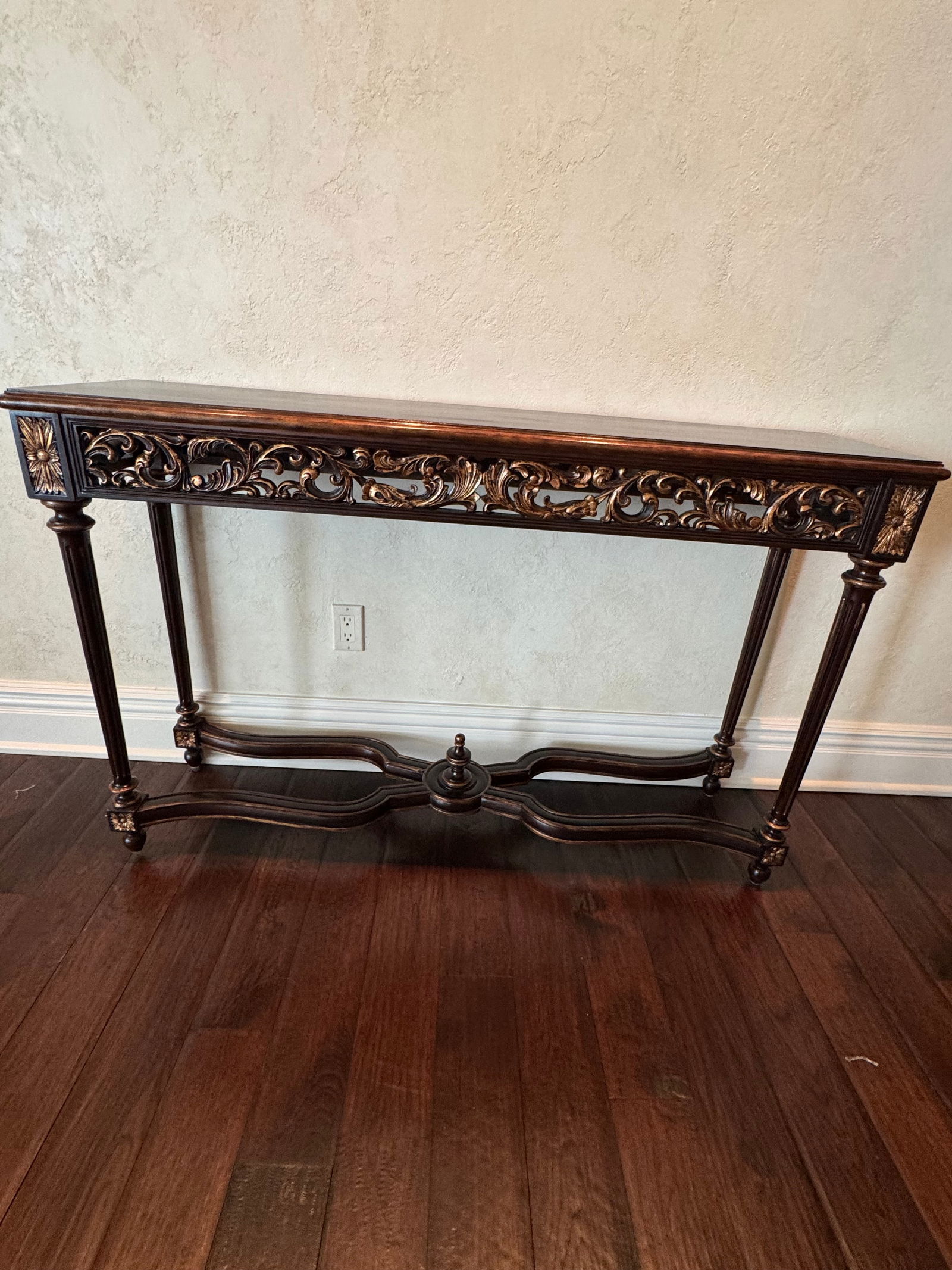 Antique Style Carved Wood Console Table with Gilded Accents: An elegant carved wood console table featuring intricate openwork floral and foliate designs across the apron, accented with gilded highlights. Raised on turned and fluted legs joined by an ornate str