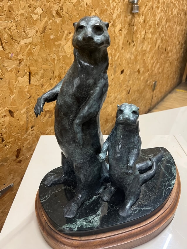 Bronze Otter Sculpture on Marble and Wood Base Wildlife Art: A finely crafted bronze sculpture depicting two otters, one larger and one smaller, standing upright in an alert pose. The figures are mounted on a polished dark green marble base with natural veining