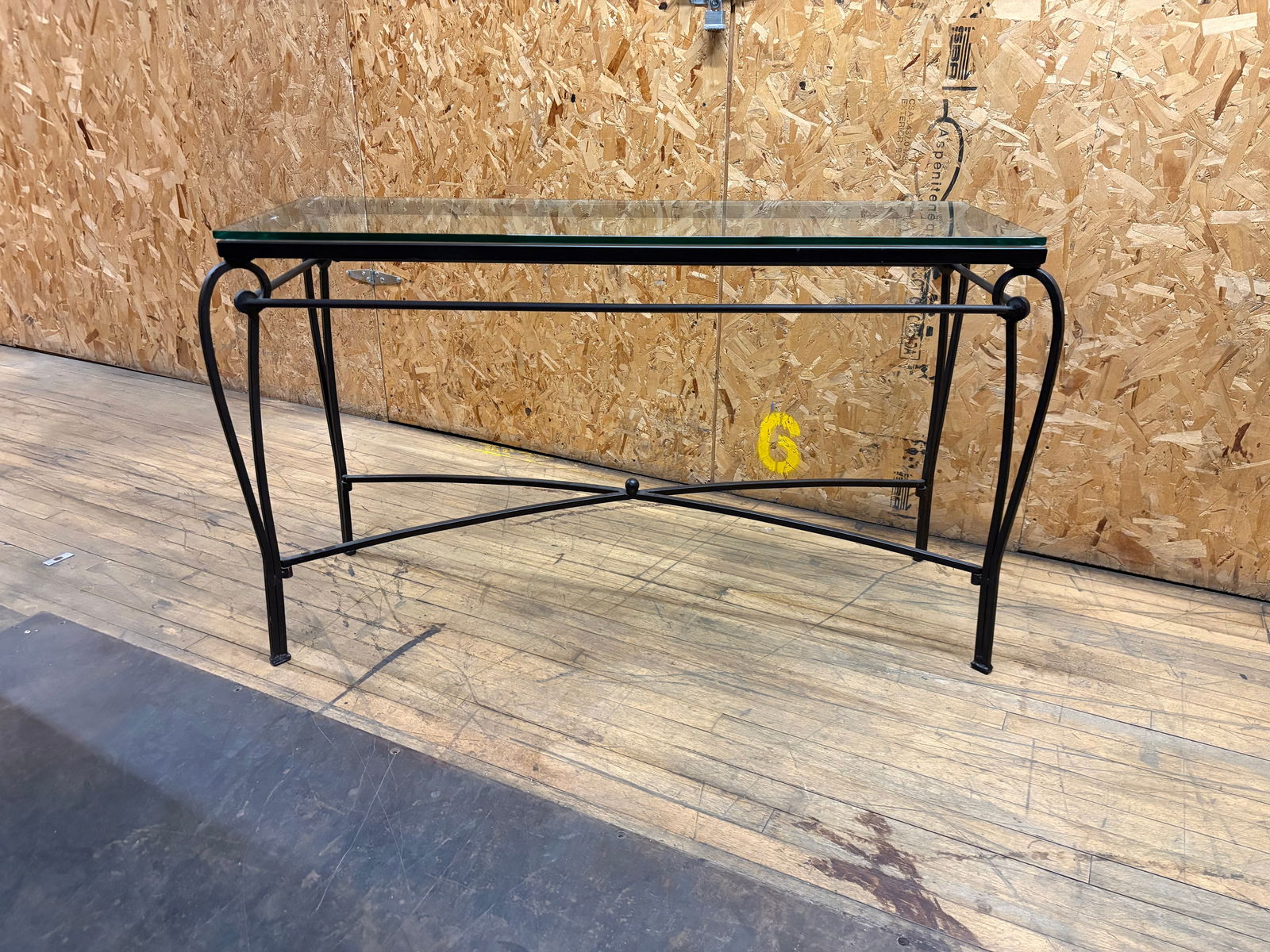 Contemporary Glass Top Console Table – Black Wrought Iron Base with Curved Legs: Elegant contemporary console table featuring a thick rectangular glass top supported by a black wrought iron base with graceful curved legs and a center stretcher for stability. The table’s design b