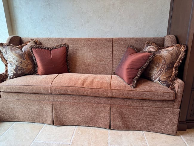 Custom Upholstered Wingback Sofa with Skirted Base and Accent Pillows: A tailored custom upholstered wingback sofa in warm brown textured fabric, featuring a straight-line skirted base and three loose seat cushions. The sofa includes four decorative accent pillows in coo