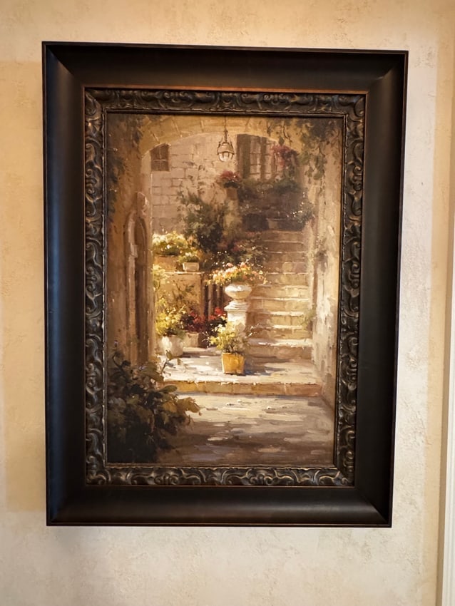 Framed Oil Painting Sunlit Courtyard with Stone Steps & Flowers: A charming oil painting depicting a sunlit courtyard scene with stone steps, blooming flowers in urns and pots, and warm architectural details. The artist captures the play of light and shadow with ri