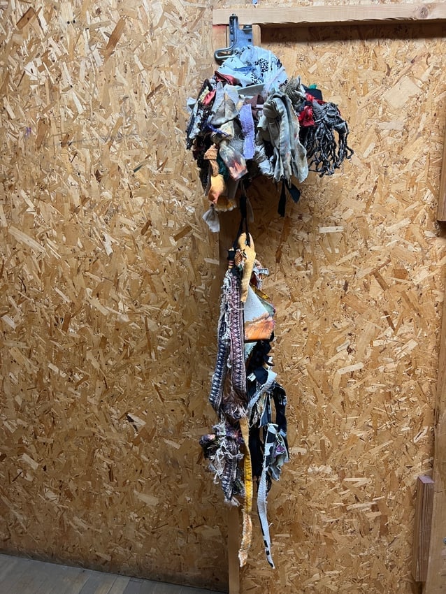Diane Cooper Untitled Textile Assemblage Mixed Media Hanging Sculpture: A tall vertical hanging assemblage by Diane Cooper, featuring layered strips of fabric, knotted rope, and found textiles cascading downward from a fabric-wrapped core. The work is crowned by a