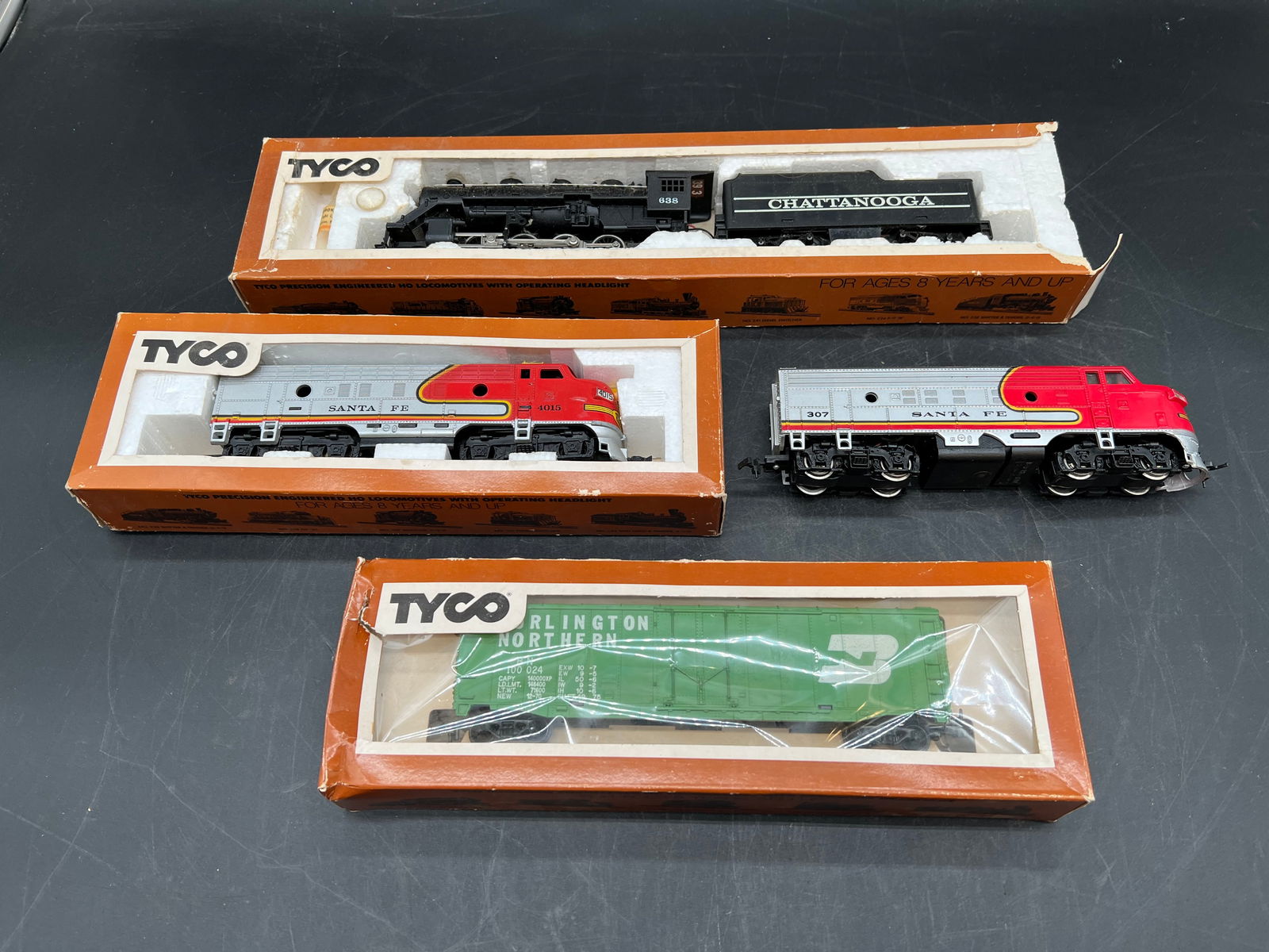 Lot of 4 Tyco HO Scale Train Engines: Lot of 4 Tyco HO Scale Train Engines. Chattanooga No. 638, Santa Fe 307, Santa Fe NO. 4015, and Burlington Northern box car. In original boxes