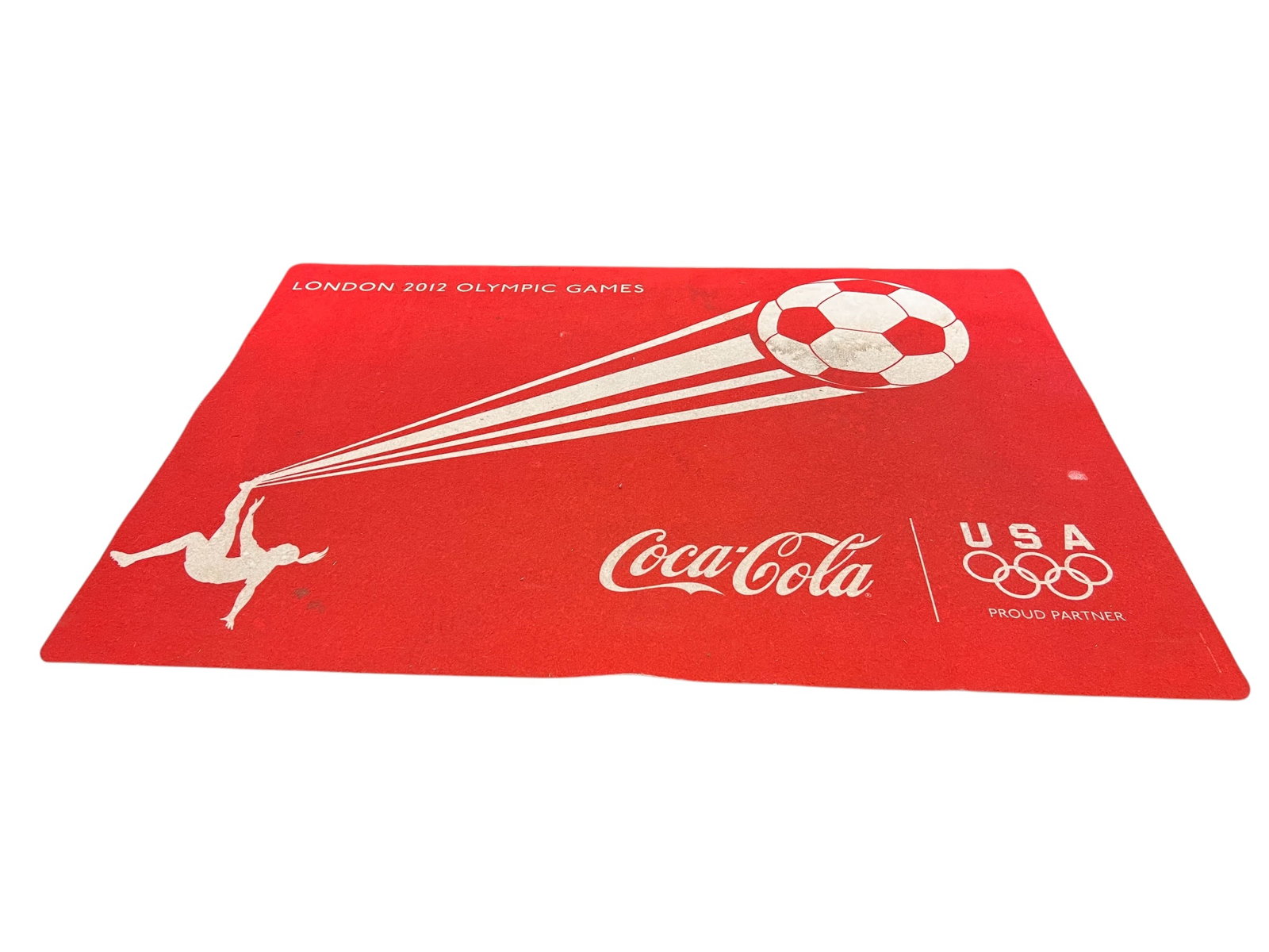London 2012 Olympic Games Mat: This image displays a London 2012 Olympic Games promotional mat featuring Coca-Cola as a proud partner of Team USA. [1, 2]Design DetailsGraphic Motif: Features the silhouette of a female soccer