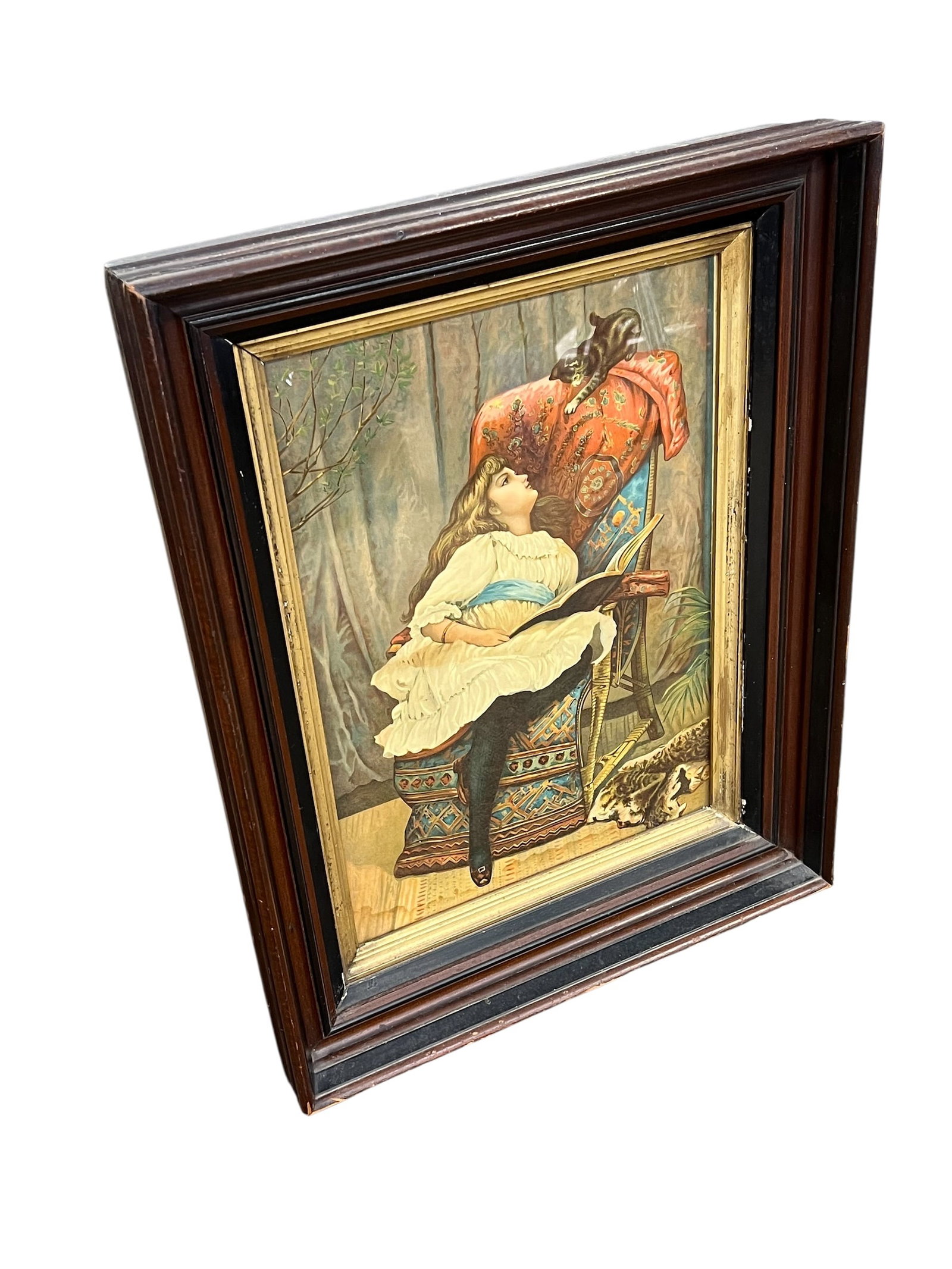 Framed Antique Print Titled Good News: This is a framed Victorian-era chromolithograph print of a girl reading. [1]Artwork Details: The print depicts a young girl in a white dress sitting in a chair and reading a book, accompanied by a