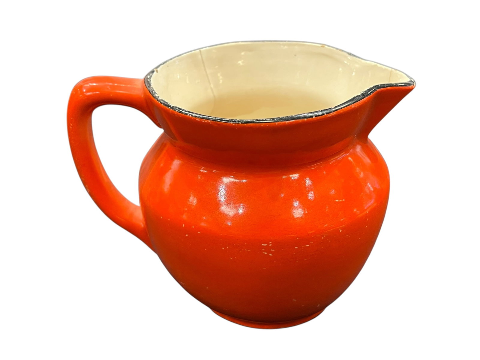 vintage Czechoslovakian pottery creamer pitcher: This item is a vintage Czechoslovakian pottery creamer pitcher, distinctively styled with a bright orange-red glaze, a cream-colored interior, and a thin black painted trim along the rim. [1, 2]Key Ch