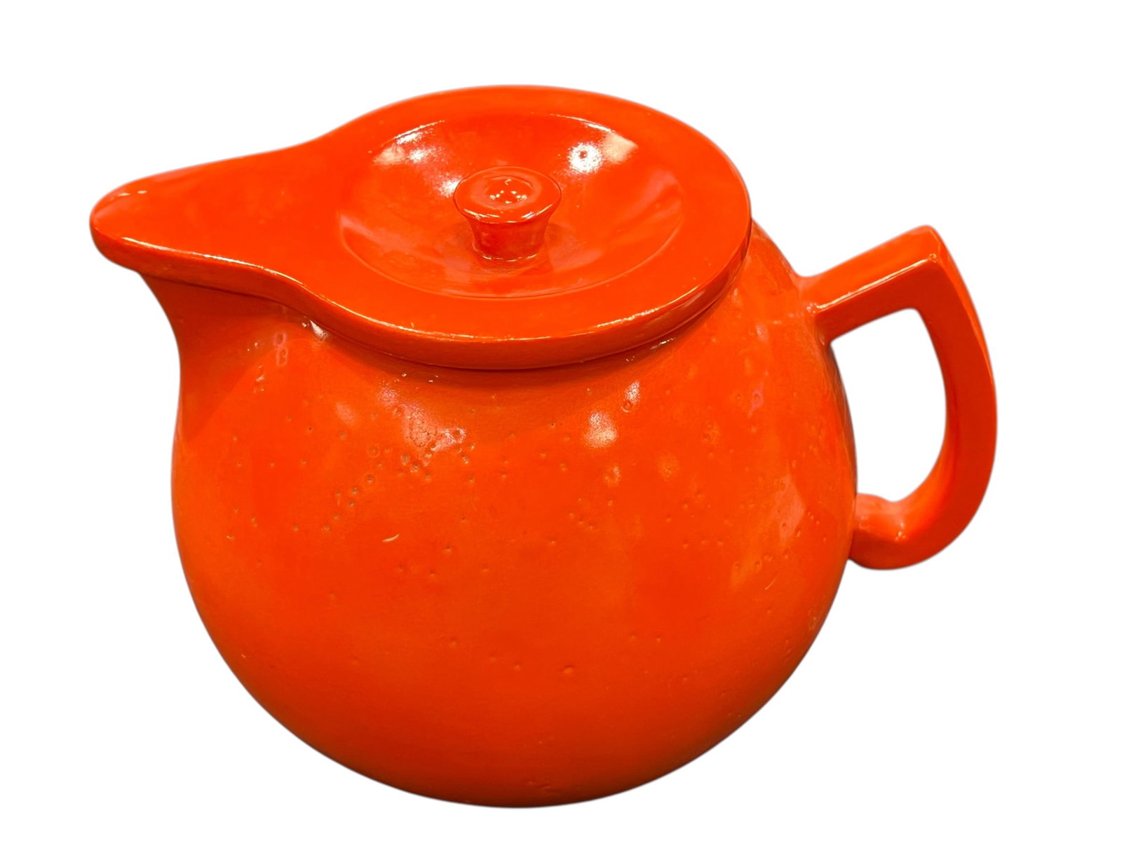 vibrant orange ceramic pitcher or teapot: This vibrant orange ceramic pitcher or teapot showcases a mid-century modern spherical silhouette paired with an integrated wide spout and an inset lid. The bold, glossy orange glaze brings a