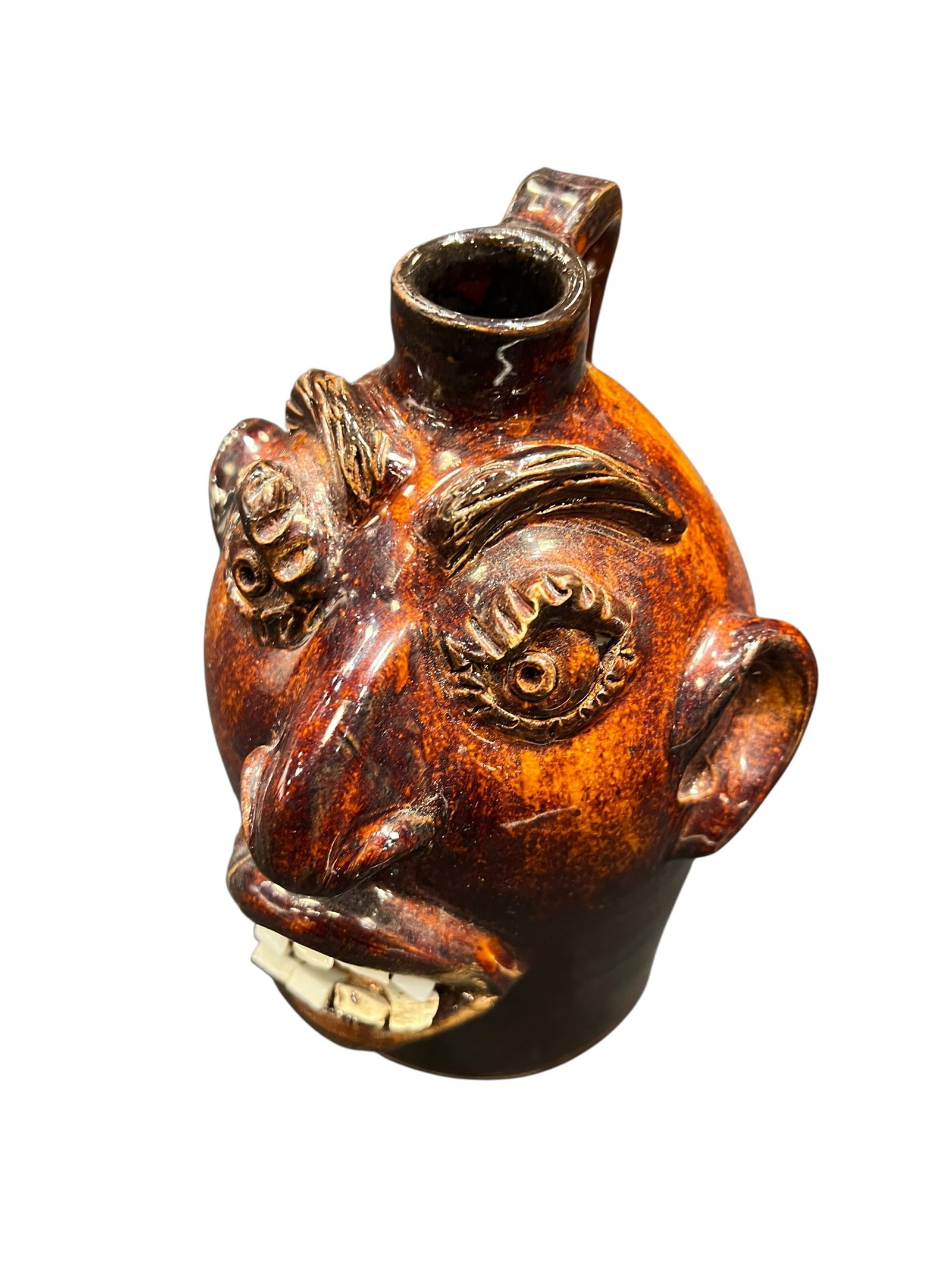 Signed Brown Pottery Face Jug: This image shows a Southern folk art pottery face jug featuring a glossy brown-orange alkaline glaze, applied clay facial features, and inlaid teeth made from broken china or stone