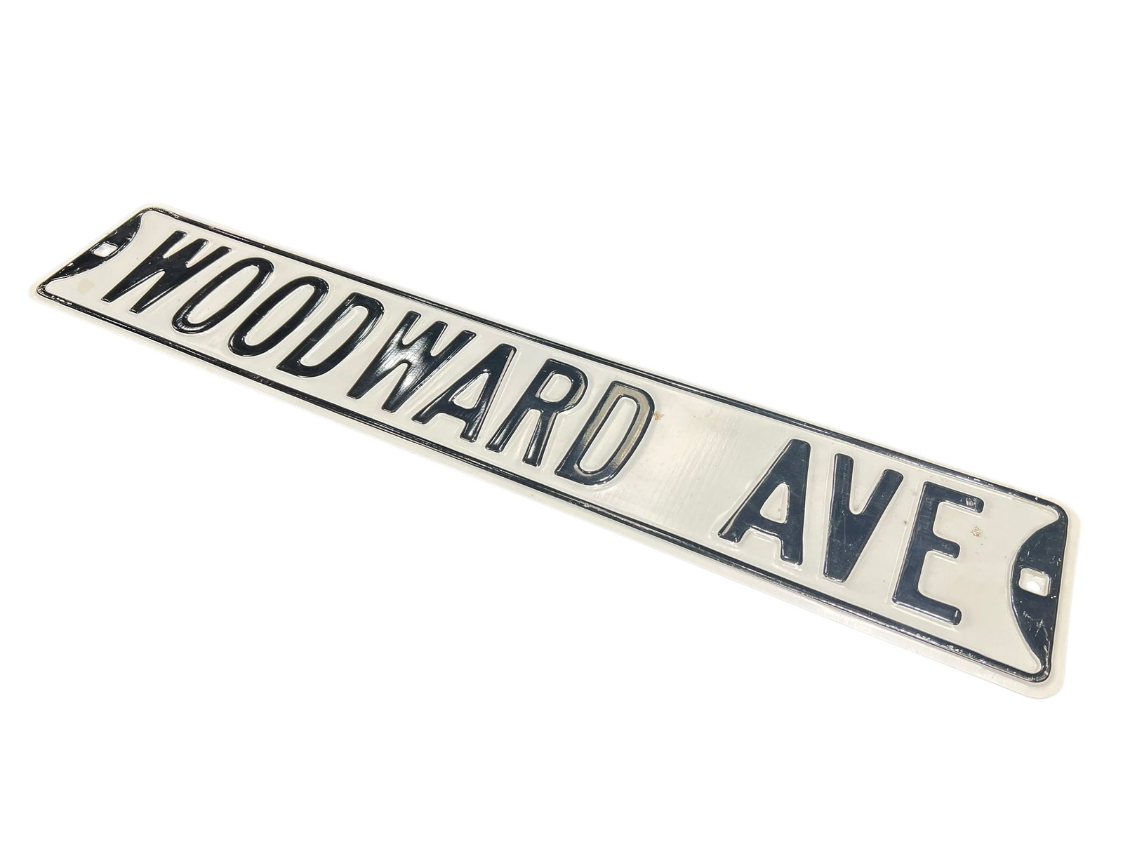 Woodward Ave Porcelain Sign: The image shows a vintage-style embossed metal street sign featuring the text "WOODWARD AVE" in black lettering on a white background. [1]Design: Raised, embossed capital lettering with a classic
