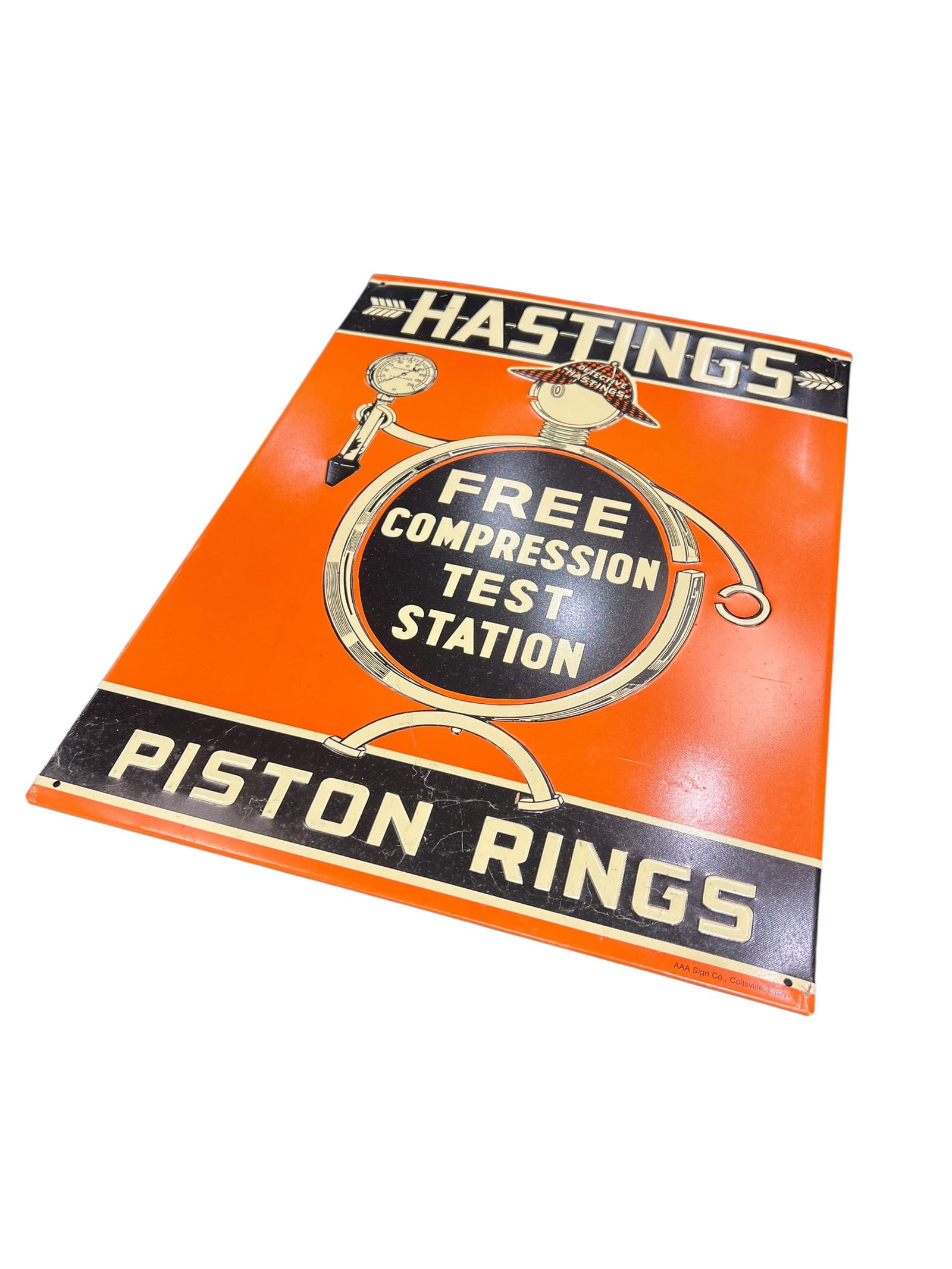 Hastings Metal Advertising Sign: This image shows a vintage single-sided or double-sided painted tin/metal advertising sign for Hastings Piston Rings, featuring a prominent "Free Compression Test Station" graphic layout. [1, 2]About 