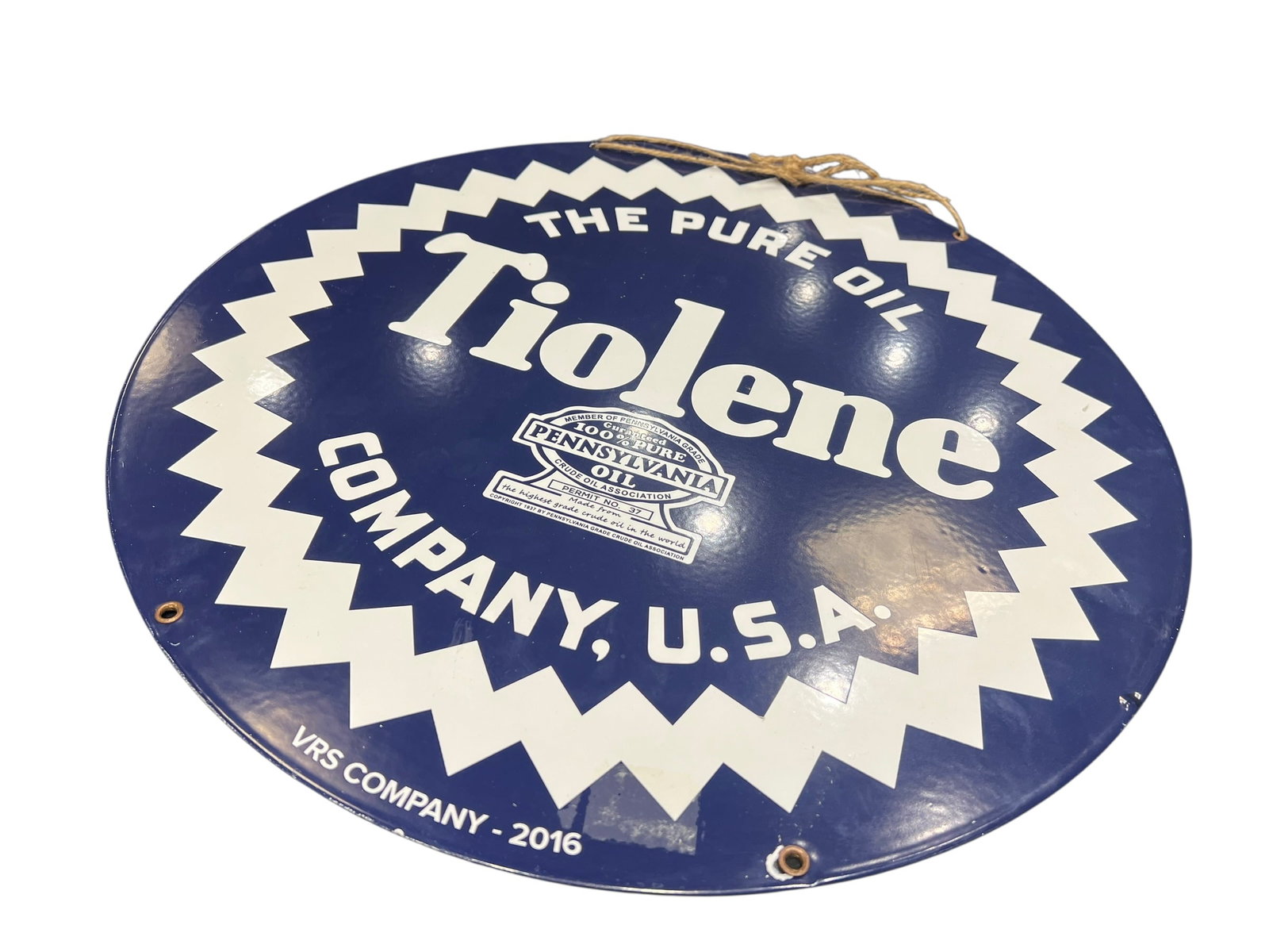 Tiolene Porcelain Advertising Sign: The object in the image is a decorative reproduction sign modeled after vintage Tiolene The Pure Oil Company advertising. However, the text near the bottom edge explicitly reads "VRS COMPANY - 2016",