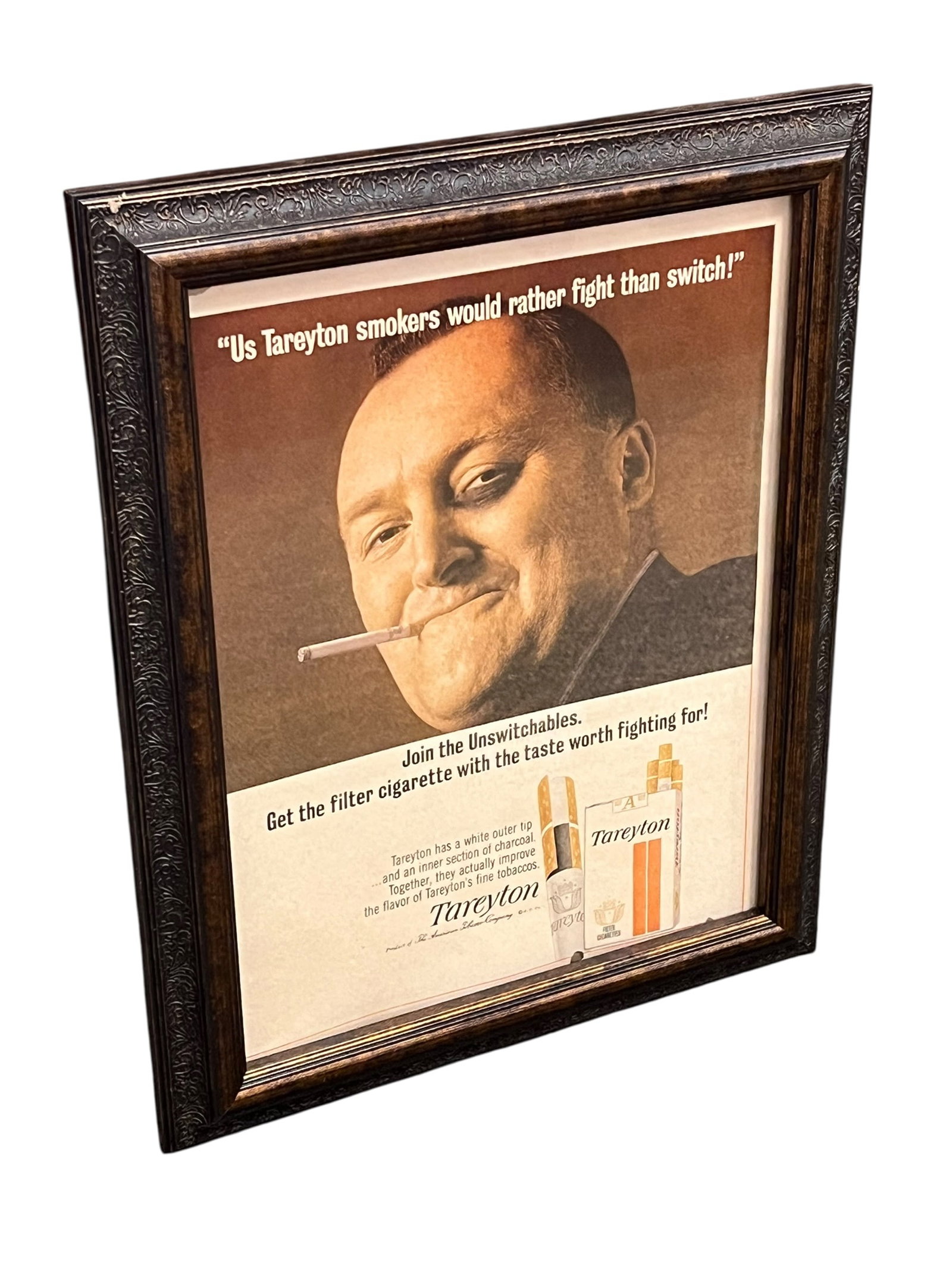 Tareyton Cigarettes Advertising Poster: This framed vintage print features a classic 1960s advertisement for Tareyton cigarettes, showcasing their iconic "Us Tareyton smokers would rather fight than switch!" campaign inside an ornate dark w