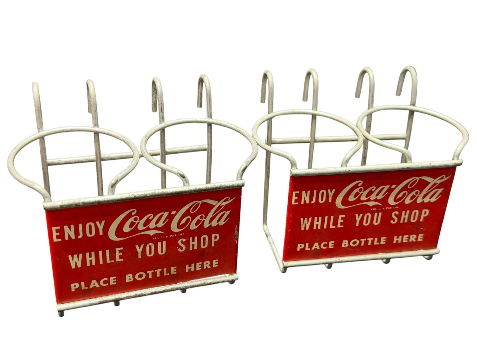 Lot of 2 Coca Cola “While You Shop?? Metal Shopping Cart Bottle Holders: These items are vintage mid-20th-century Coca-Cola "While You Shop" metal shopping cart bottle holders/carriers. [1, 2]OverviewDesign: White-coated iron wire framing with red lithographed metal advert